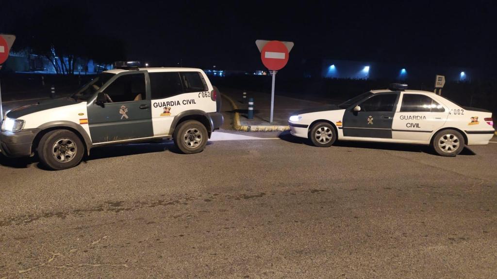 Dos vehículos de la Guardia Civil estacionados de noche frente a una señal de dirección prohibida, en una carretera con iluminación tenue y edificios al fondo, durante un operativo.