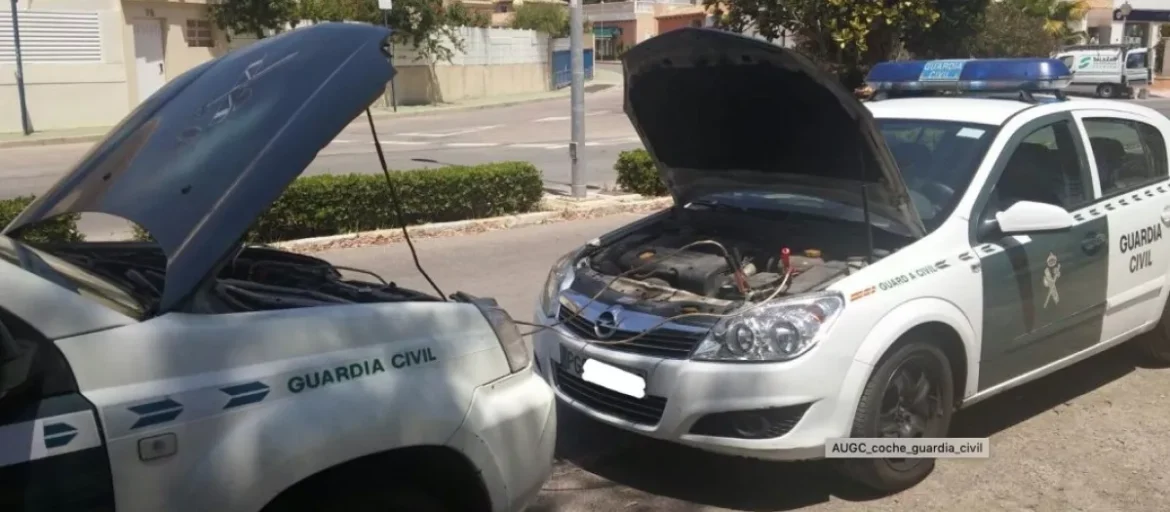 Dos vehículos patrulla de la Guardia Civil con el capó levantado, realizando una recarga de batería, lo que evidencia el desgaste y la falta de mantenimiento en la flota oficial, según la denuncia de JUCIL sobre la gestión del Ministerio del Interior.