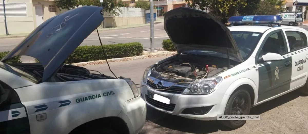 Dos vehículos patrulla de la Guardia Civil con el capó levantado, realizando una recarga de batería, lo que evidencia el desgaste y la falta de mantenimiento en la flota oficial, según la denuncia de JUCIL sobre la gestión del Ministerio del Interior.