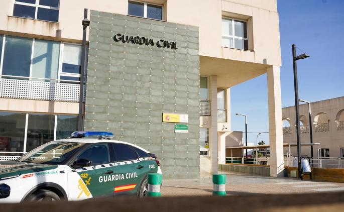 Vehículo de la Guardia Civil estacionado frente a una comisaría, con el logo de la institución claramente visible en la fachada del edificio.
