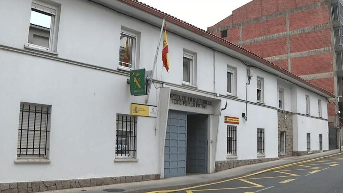 Fachada del cuartel de la Guardia Civil en Carballo, con la bandera de España ondeando sobre el portón de entrada y varios ventanales enrejados a pie de calle.