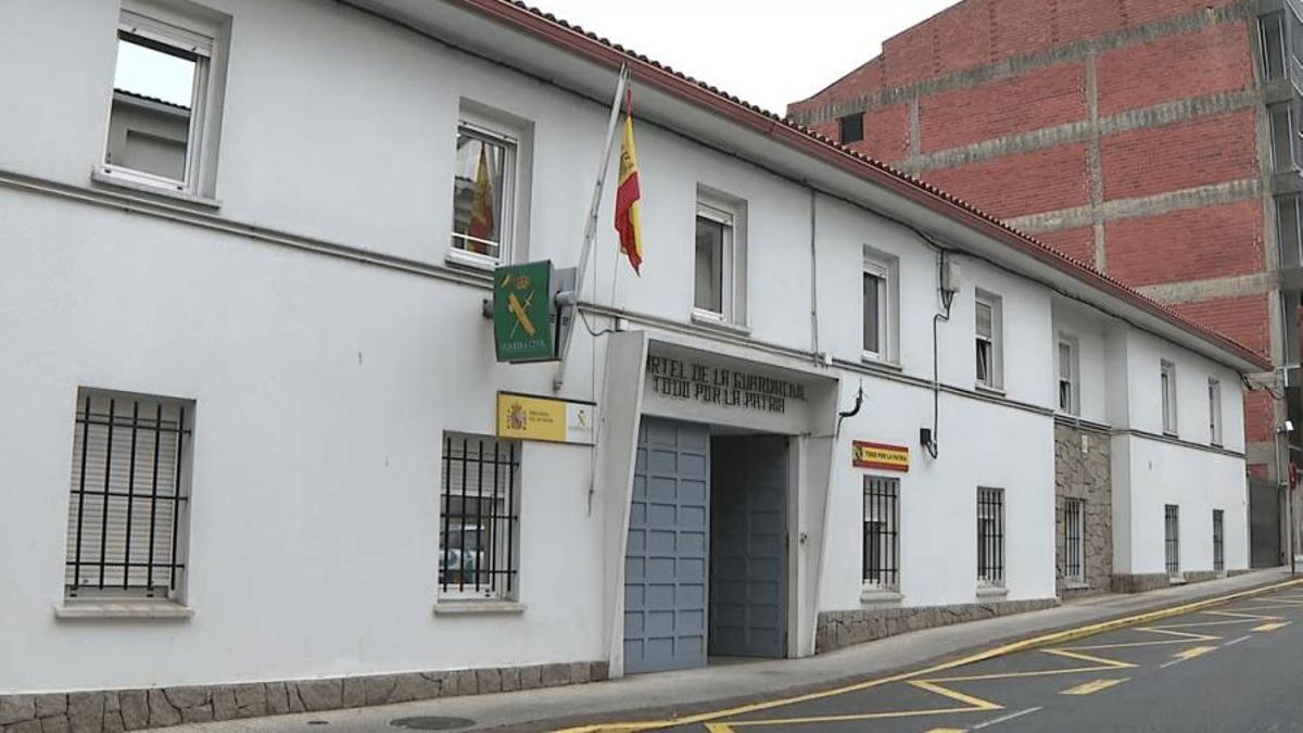 Fachada del cuartel de la Guardia Civil en Carballo, con la bandera de España ondeando sobre el portón de entrada y varios ventanales enrejados a pie de calle.