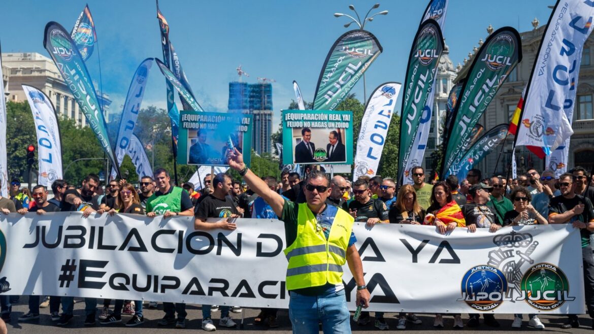 Manifestación de JUCIL con pancartas de "Equiparación Ya" y banderas de la Guardia Civil frente a edificios modernos, con personas vestidas de verde y chalecos reflectantes alzando los brazos.