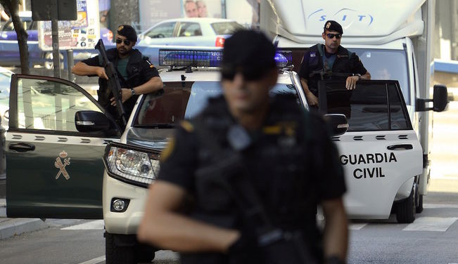 Agentes de la Guardia Civil del GRS en operación urbana, con chalecos tácticos, armas largas y vehículos policiales con luces azules en una calle con peatones y anuncios publicitarios.