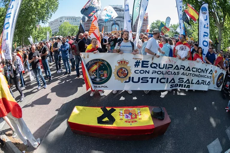 Manifestación de policías y guardias civiles en Madrid con pancarta de JUSAPOL reclamando equiparación salarial con las policías autonómicas y una jubilación digna, frente a un féretro simbólico con la bandera de España.